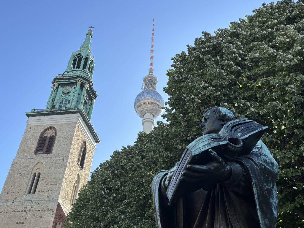 Eine Statue Martin Luthers, der ein Buch vor dem Turm der Marienkirche hält. Hinter dem Kirchturm ist der Fernsehturm Berlin sichtbar.